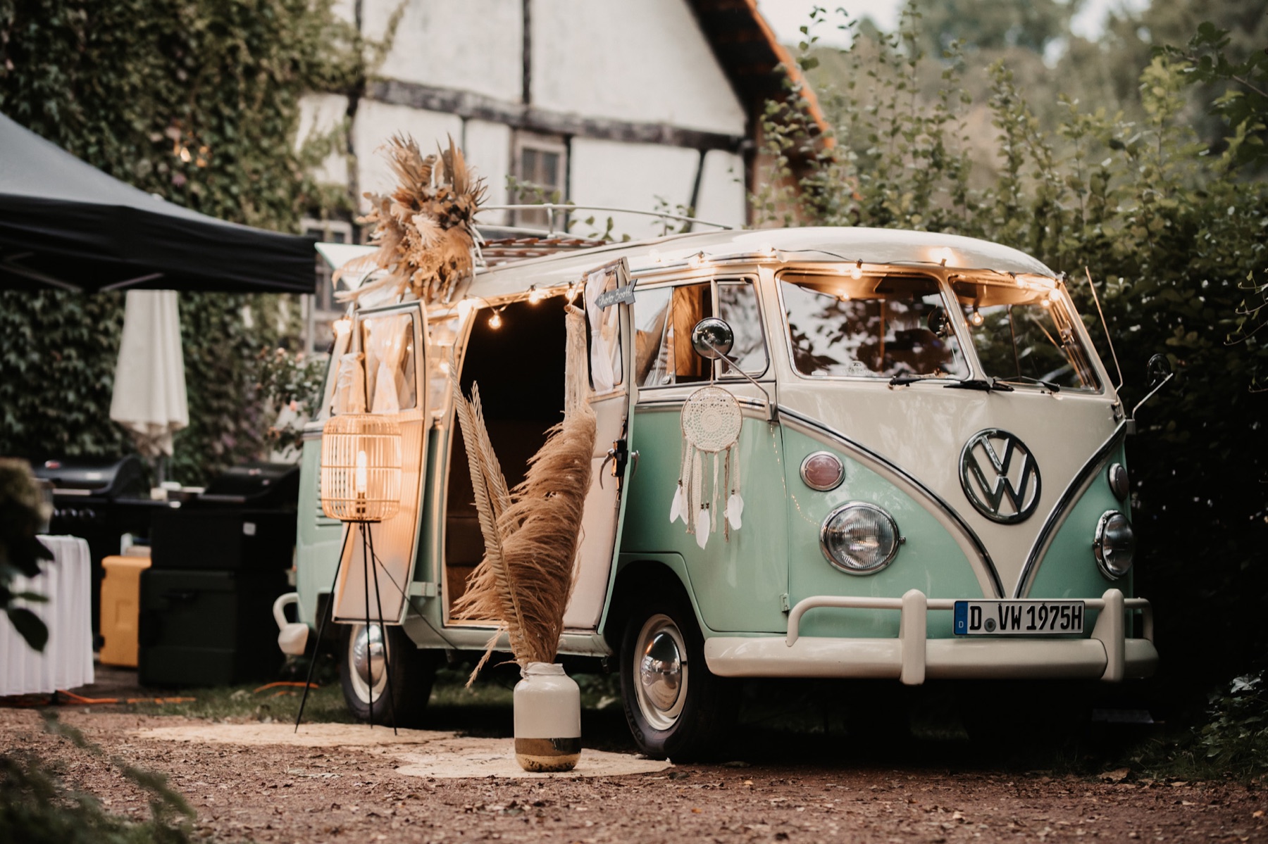 Mintgrüner VW T1 Fotobulli, boho-dekoriert mit geöffneten Türen vor einem Fachwerkhaus
